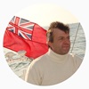 A man wearing a white turtleneck with a red flag behind him, old photo