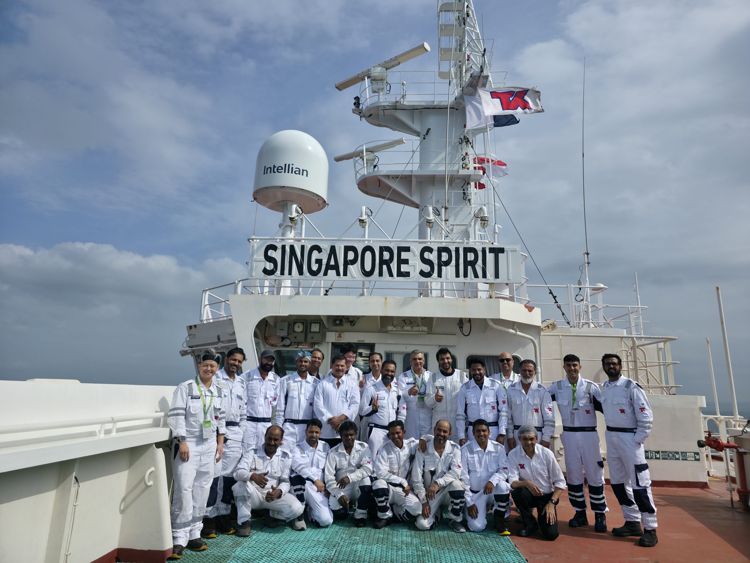 Employees in white coveralls posing as a group under the Singapore Spirit sign